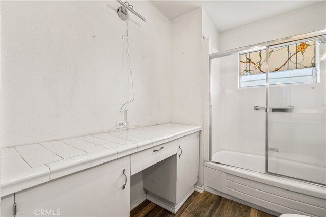 bathroom with bath / shower combo with glass door and wood-type flooring