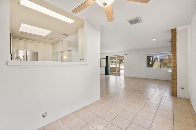 empty room featuring light tile patterned floors, a skylight, and ceiling fan