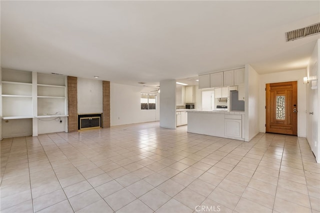 unfurnished living room with a brick fireplace, visible vents, a ceiling fan, and light tile patterned flooring