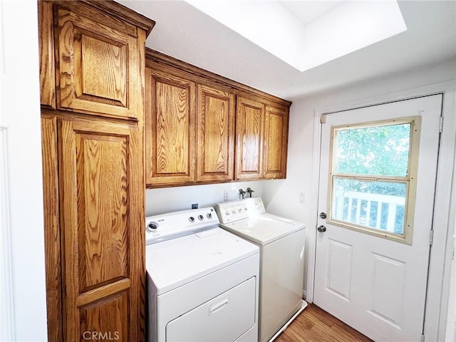 clothes washing area with cabinets, washer and clothes dryer, and light hardwood / wood-style flooring