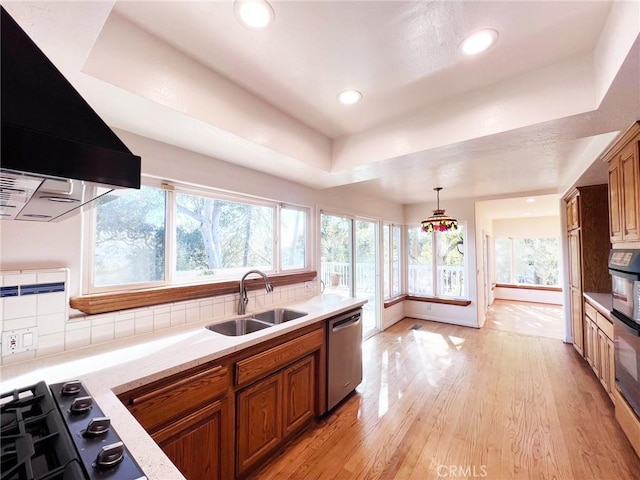 kitchen with pendant lighting, dishwasher, sink, exhaust hood, and light wood-type flooring