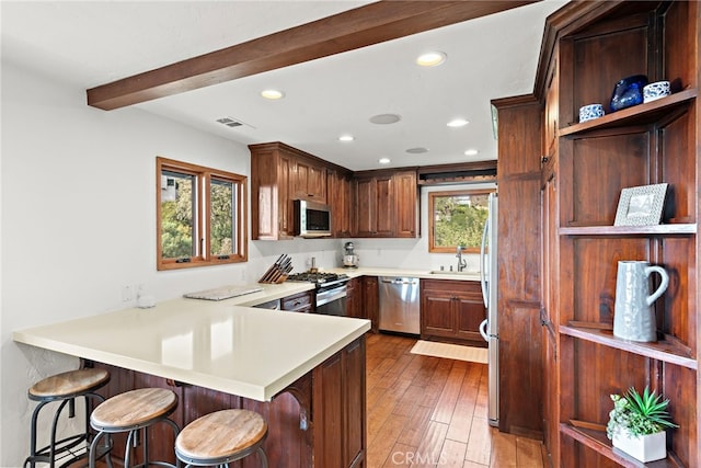 kitchen with appliances with stainless steel finishes, a kitchen bar, kitchen peninsula, and light hardwood / wood-style floors