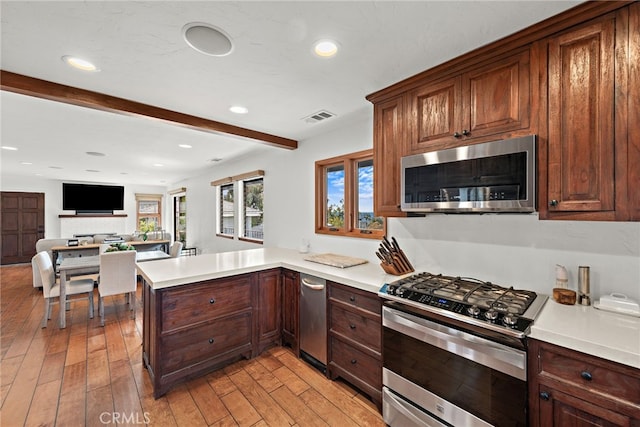 kitchen with beamed ceiling, stainless steel appliances, kitchen peninsula, and light hardwood / wood-style flooring