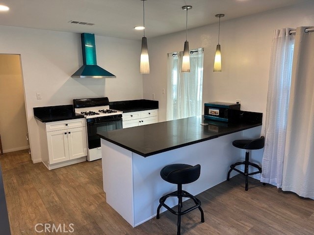 kitchen with white range with gas cooktop, white cabinetry, decorative light fixtures, and wall chimney exhaust hood