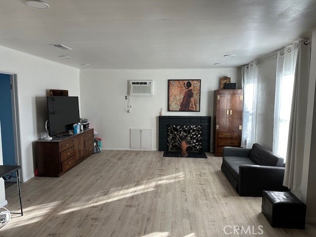 living room with a wall mounted air conditioner, a fireplace, and light hardwood / wood-style floors