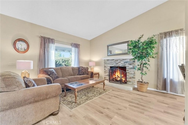 living room with a tiled fireplace, plenty of natural light, light hardwood / wood-style floors, and vaulted ceiling