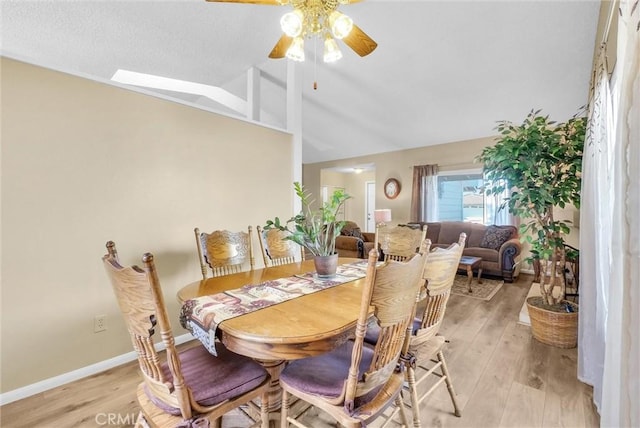 dining space featuring ceiling fan, lofted ceiling with skylight, and light wood-type flooring