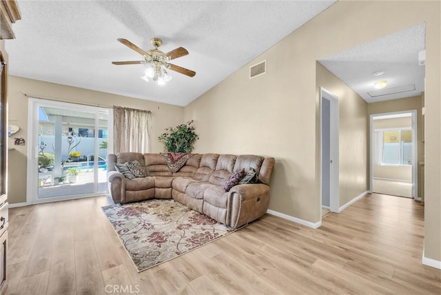 living room with ceiling fan, lofted ceiling, a textured ceiling, and light wood-type flooring