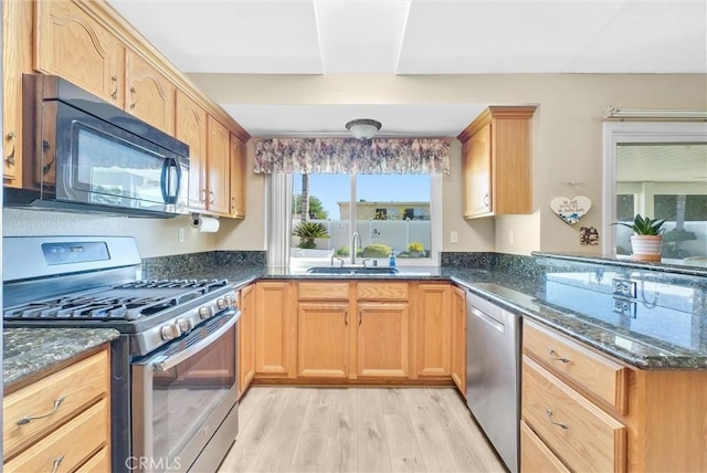 kitchen with appliances with stainless steel finishes, sink, dark stone countertops, and light hardwood / wood-style floors