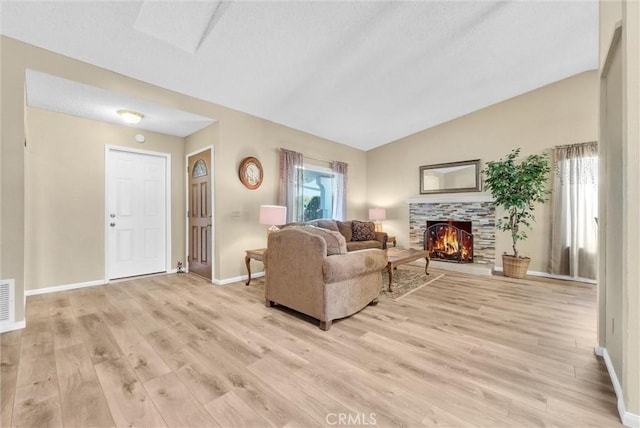 living room featuring vaulted ceiling, plenty of natural light, a fireplace, and light hardwood / wood-style flooring