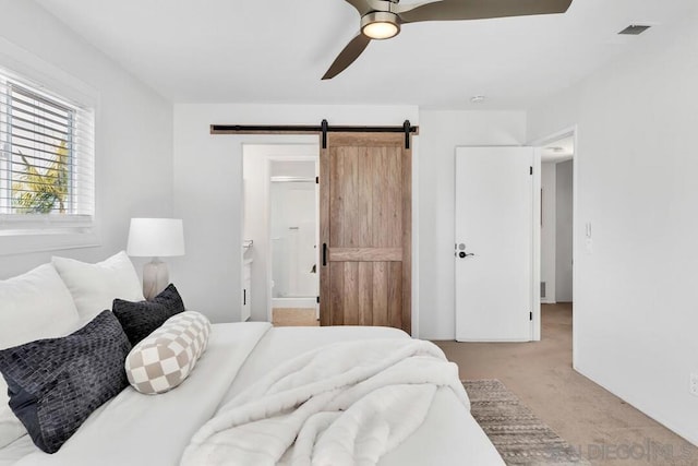 bedroom with ensuite bathroom, a barn door, light carpet, and ceiling fan