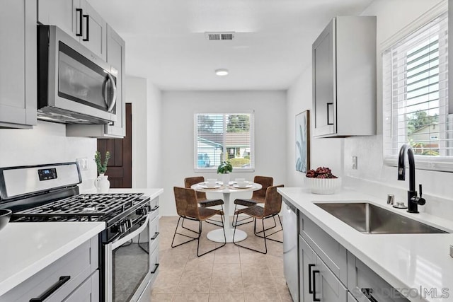 kitchen with light tile patterned flooring, appliances with stainless steel finishes, gray cabinets, and sink