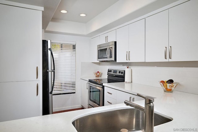 kitchen with tasteful backsplash, sink, white cabinets, and appliances with stainless steel finishes