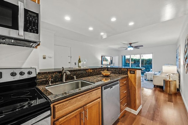 kitchen with wood-type flooring, appliances with stainless steel finishes, sink, and dark stone countertops