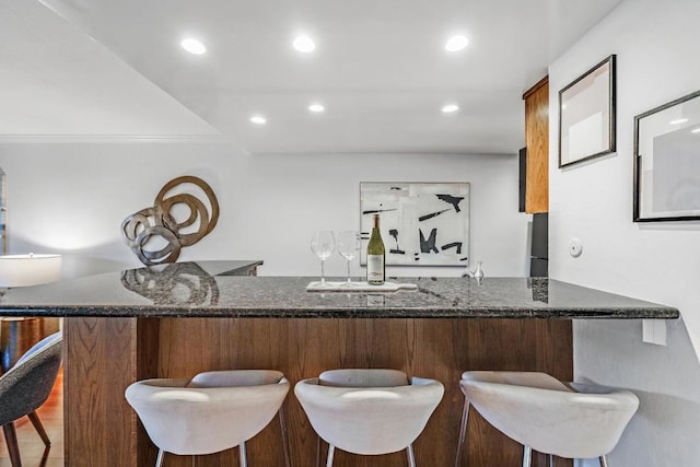 bar with dark stone countertops and ornamental molding