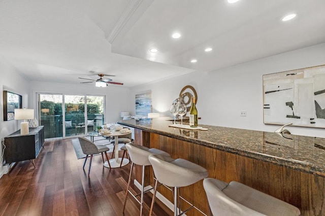 kitchen with crown molding, dark wood-type flooring, dark stone countertops, and ceiling fan