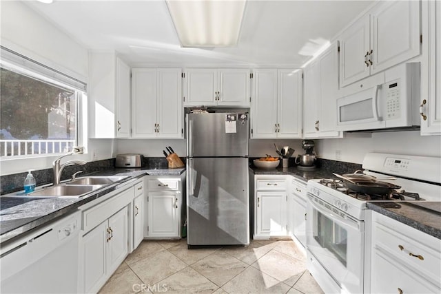 kitchen featuring sink, white appliances, light tile patterned floors, white cabinetry, and dark stone countertops