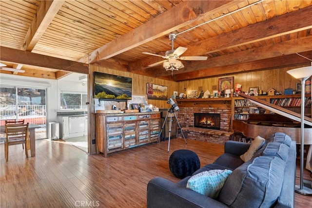 living room with beamed ceiling, wooden ceiling, ceiling fan, and wood walls