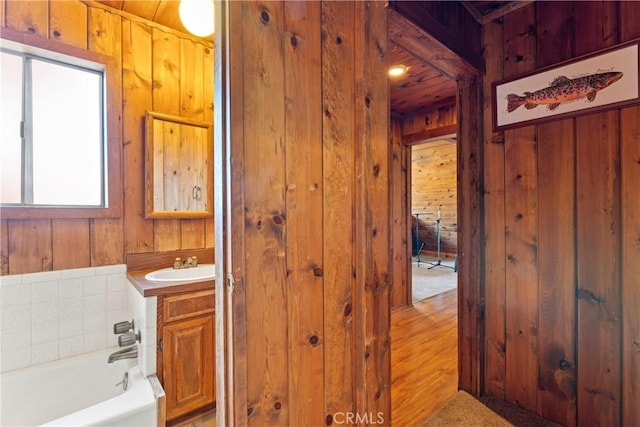 bathroom featuring vanity, wooden walls, and a bath