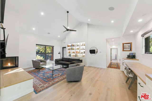 living room with a wealth of natural light, light hardwood / wood-style flooring, high vaulted ceiling, and a multi sided fireplace