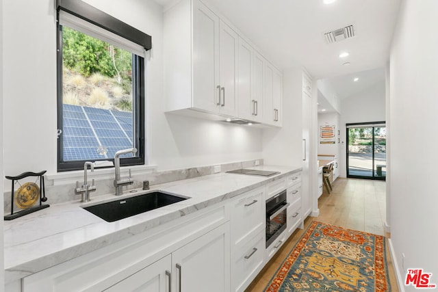 kitchen featuring white cabinetry, oven, sink, and light stone counters