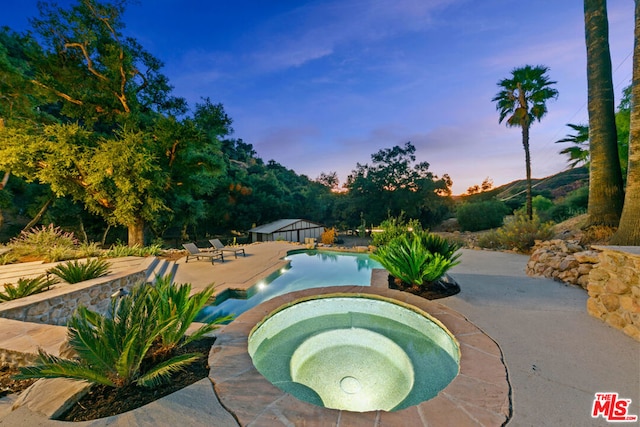 pool at dusk with an in ground hot tub and a patio area