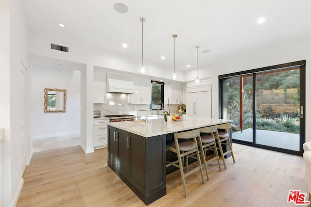 kitchen with paneled built in refrigerator, custom range hood, white cabinets, pendant lighting, and backsplash