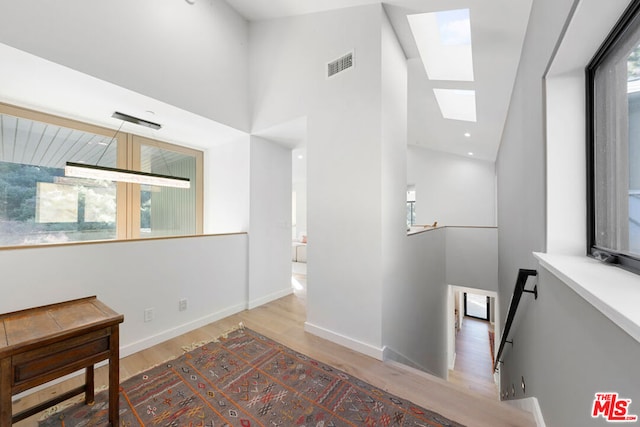 corridor with a towering ceiling, a skylight, and light hardwood / wood-style floors