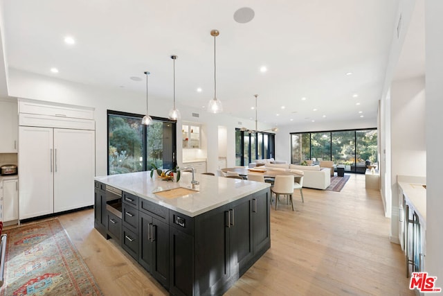 kitchen with sink, hanging light fixtures, paneled refrigerator, a wall of windows, and a kitchen island with sink