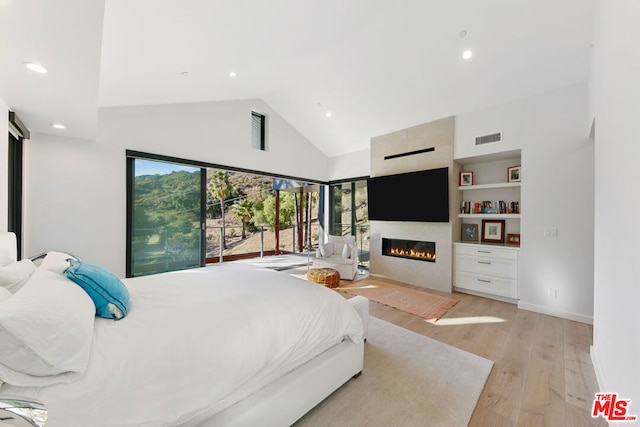 bedroom with a large fireplace, high vaulted ceiling, and light hardwood / wood-style floors