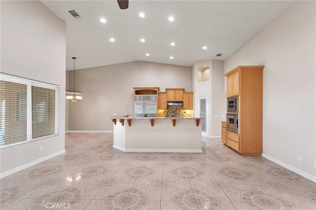 kitchen featuring a breakfast bar area, a kitchen island with sink, built in appliances, decorative backsplash, and decorative light fixtures