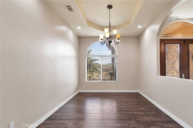 unfurnished dining area featuring dark hardwood / wood-style floors, a tray ceiling, and a chandelier