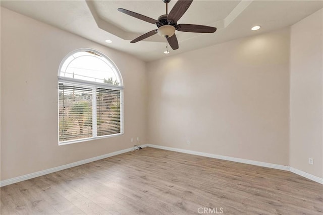 empty room with a tray ceiling, ceiling fan, and light wood-type flooring