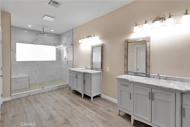 bathroom featuring hardwood / wood-style flooring, tiled shower, and vanity