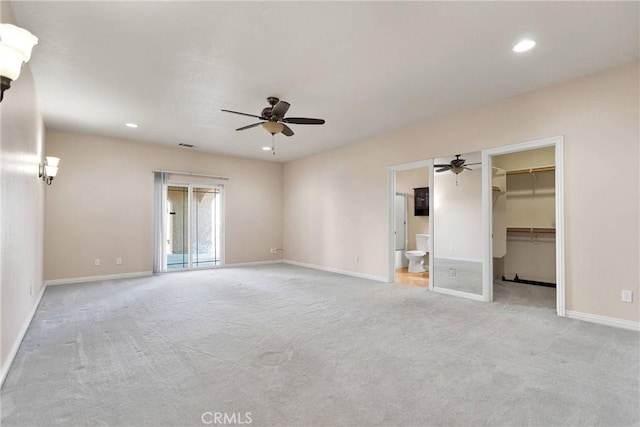 unfurnished bedroom with light carpet, a spacious closet, ceiling fan, and ensuite bathroom