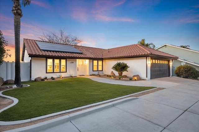 view of front of property featuring a garage, a lawn, and solar panels