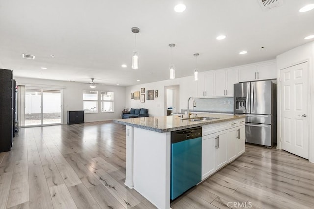 kitchen with decorative light fixtures, white cabinets, light stone counters, stainless steel appliances, and a center island with sink