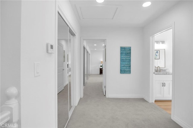 hall featuring attic access, baseboards, light colored carpet, a sink, and recessed lighting