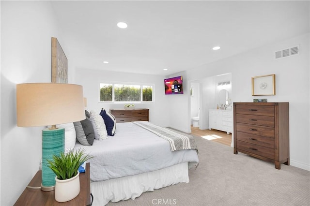 bedroom with connected bathroom and light colored carpet