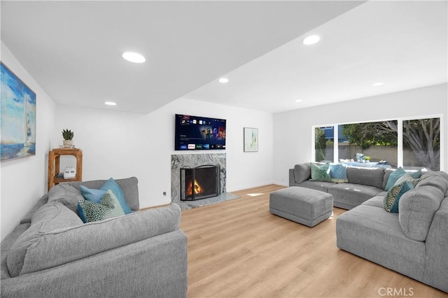 living room with baseboards, light wood-type flooring, a high end fireplace, and recessed lighting