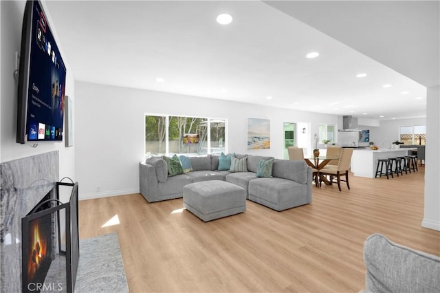 living room featuring a fireplace with flush hearth, baseboards, light wood-style flooring, and recessed lighting