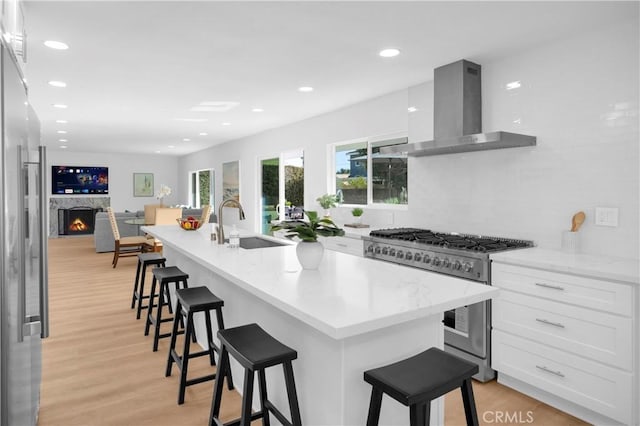 kitchen featuring a breakfast bar area, a sink, white cabinetry, appliances with stainless steel finishes, and wall chimney exhaust hood