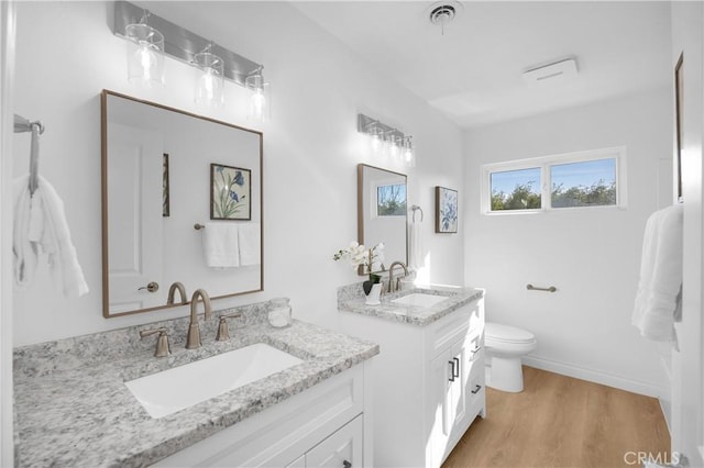 full bathroom featuring two vanities, a sink, toilet, and wood finished floors