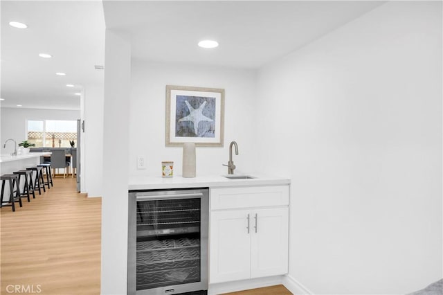 bar featuring white cabinets, sink, beverage cooler, and light hardwood / wood-style floors