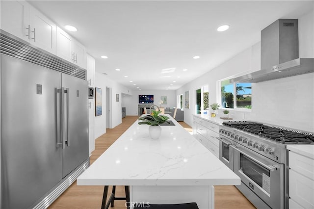 kitchen featuring high quality appliances, white cabinetry, a center island, and wall chimney exhaust hood