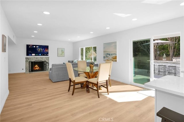 dining room featuring baseboards, light wood-type flooring, a high end fireplace, and recessed lighting