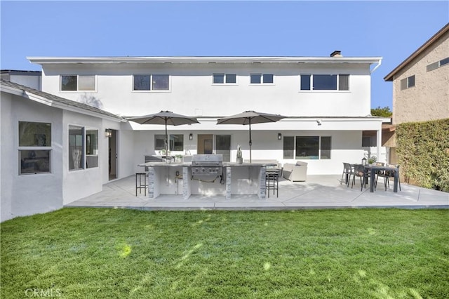 rear view of property with a yard, a patio, stucco siding, a bar, and exterior kitchen