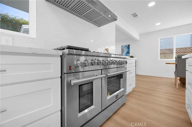 kitchen with white cabinetry, wall chimney range hood, light wood-type flooring, and double oven range