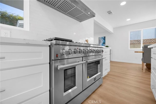 kitchen featuring light wood finished floors, visible vents, range with two ovens, white cabinets, and wall chimney range hood