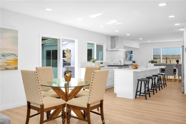 kitchen featuring wall chimney range hood, white cabinetry, a kitchen island with sink, a kitchen breakfast bar, and light wood-type flooring